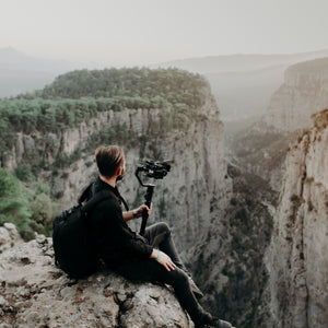 Man holding tripod with camera looking over mountain range