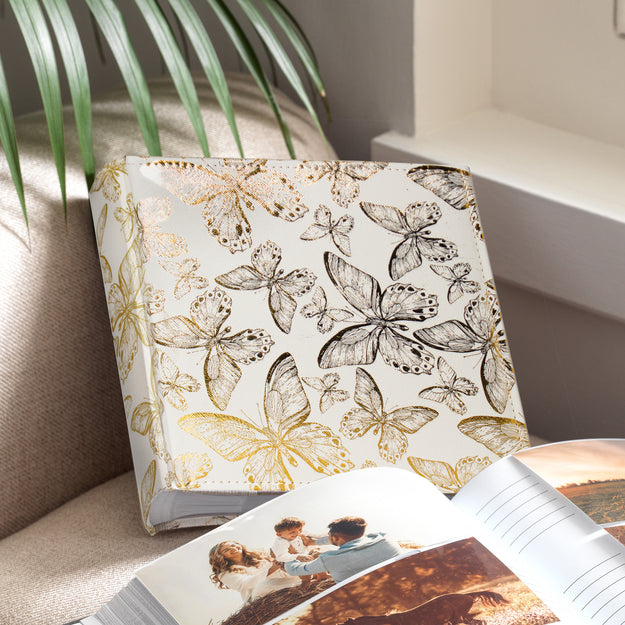 Photo album with gold foil butterfly design on a surface next to an open album