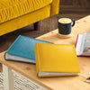 Two photo albums, one blue and one yellow, on a wooden table with a cup of coffee in the background.