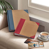 Two photo albums on a couch with a cup of coffee and saucer, and a plant in the background.